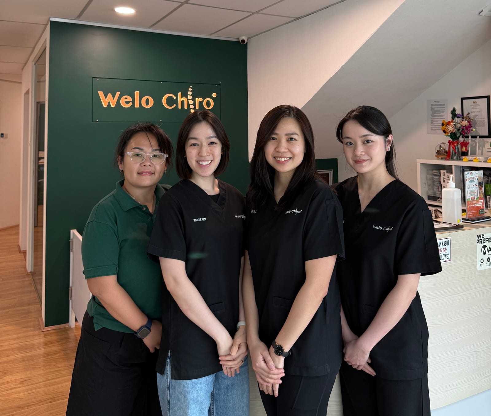 Four members of the Welo Chiro team at the Damansara Jaya reception, in front of the Welo Chiro sign